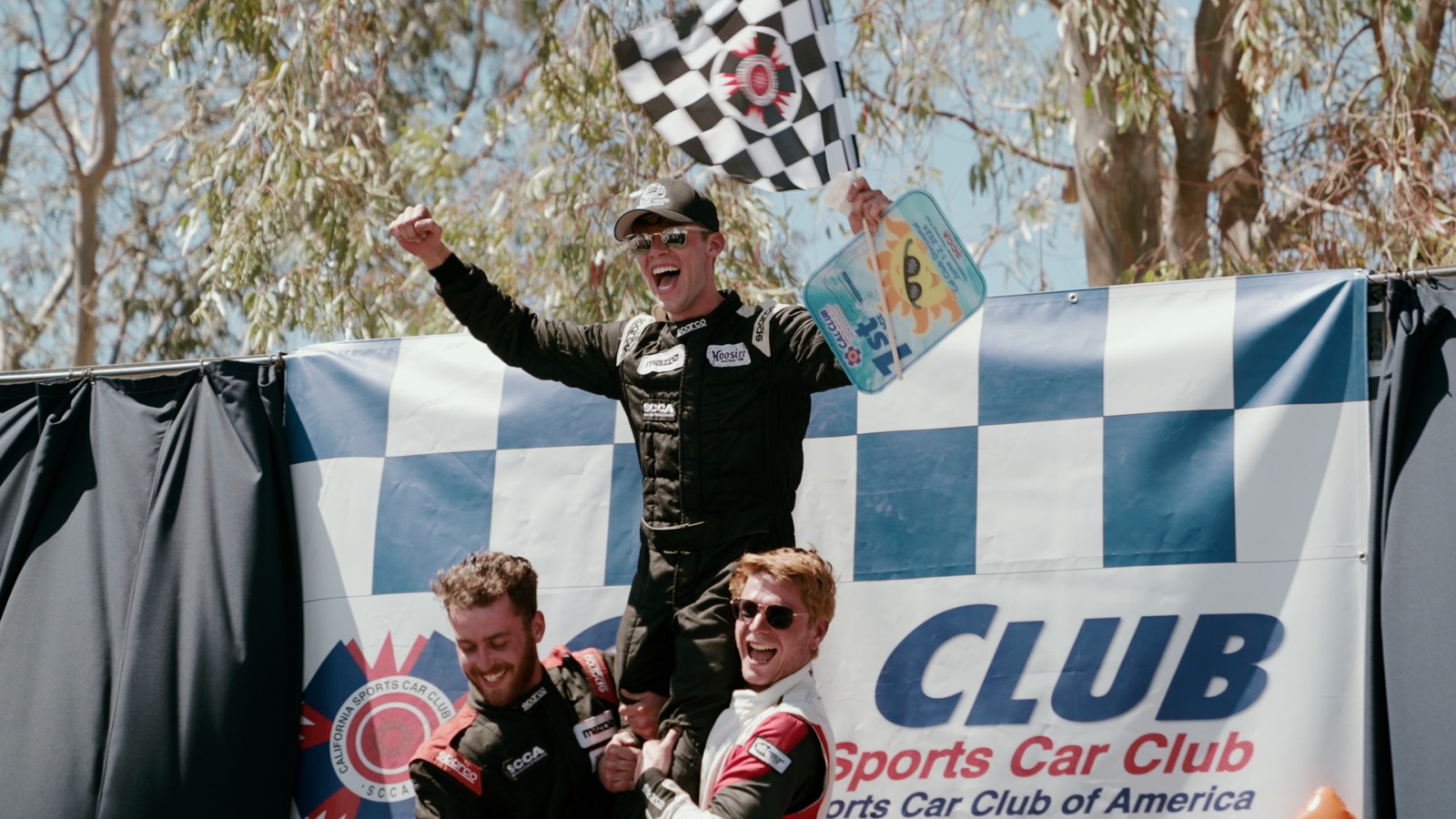 Ren celebrating on an SCCA podium with the checkered flag